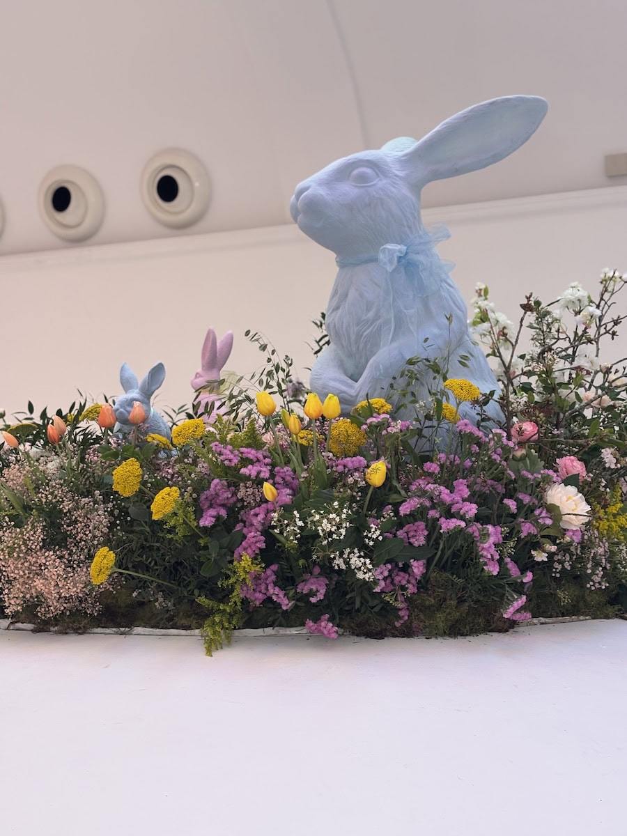 Blue Bunny Sculpture In A Floral Landscape With Pastel Spring Blooms