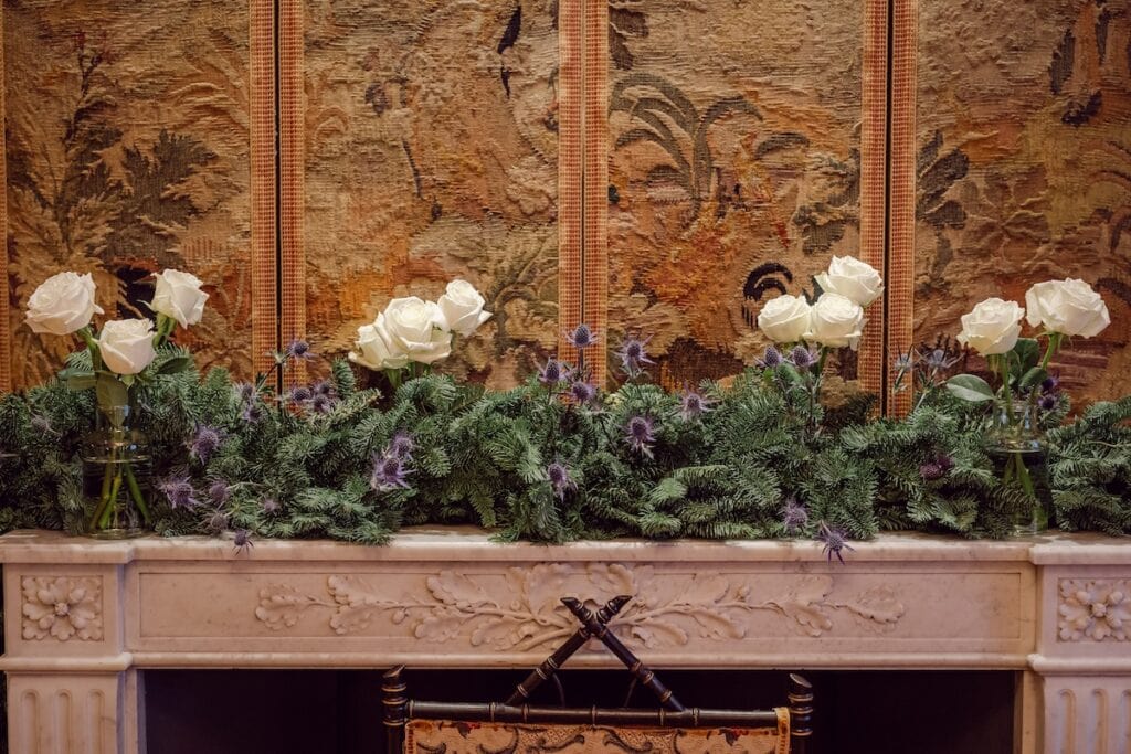 A festive garland of pine, white roses, and thistles styled on a marble fireplace, adding to the seasonal romance of the wedding setting