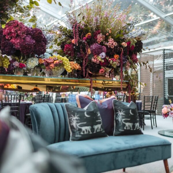 Blue velvet sofa with illustrated pillows beneath a vibrant floral installation at a luxury wedding event